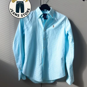 Ljusblå skjorta från Ralph Lauren - Snygg ljusblå skjorta från Ralph Lauren i slim fit-modell. Skjortan är tillverkad i 100% bomull, har klassisk krage, långa ärmar och knappar framtill. Ikoniska broderade loggan på bröstet ger en clean och stilren look. Sitter som storlek XS