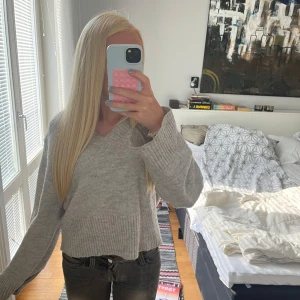 Grå stickad v-ringad tröja - Mysig grå stickad tröja med v-ringning och breda ribbade armar. Tröjan har en loose passform och långa ärmar. 