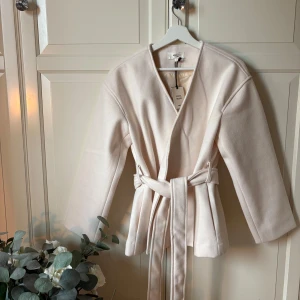 Beige kappa med bälte  - Snygg beige kappa från Gina. Aldrig använd och alla lappar kvar. Perfekt till höst och vår.