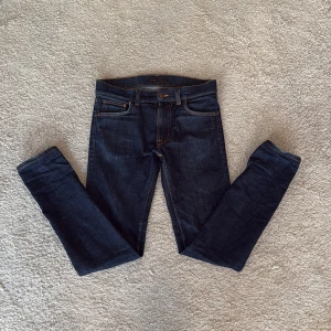 Mörkblå Nudie Jeans Lean Dean - Ovanliga mörkblå slim jeans från Nudie Jeans med klassisk femficksdesign och kontrastsömmar, köpta på Jeansbolaget. Modellen har smal passform och raka ben, tillverkade i slitstarkt jeanstyg. Perfekt för dig som gillar en stilren och modern look.