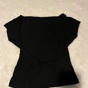 Svart offshoulder topp i bomull - En svart offshoulder topp med korta ärmar och figurnära passform. Tillverkad i mjuk bomull, perfekt för en stilren och enkel look. Toppen har en klassisk, minimalistisk design utan mönster eller extra detaljer.