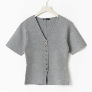 Grå v-ringad topp från Gina Tricot - Grå kortärmad topp från Gina Tricot med v-ringning och snygga knappar framtill. Modellen är figurnära och har en stilren, enkel design som passar perfekt till jeans eller kjol. Mjuk och bekväm känsla tack vare det stickade materialet. Tröjan har endast används 1 gång