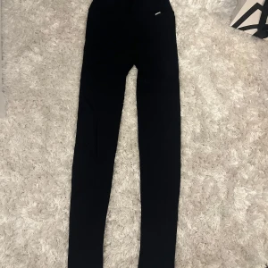 Svarta leggings från Stronger - Svarta leggings från Stronger med ribbade detaljer längs benen. De är tighta och har hög midja, perfekta för träning eller chill. Materialet är stretchigt och mjukt för maximal komfort.