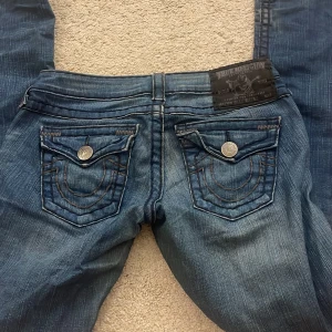 True Religion blå bootcut jeans - Säljer ett par blå jeans från True Religion med bootcut passform. Midjemåttet är 39 och innerbenslängden 84❤️ säljer pga de inte passar längre tyvärr💔som man kan se så är de lite upptrampade men inget som syns eller känns 