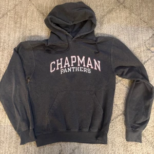 Mörkgrå Chapman Panthers hoodie Champion - Säljer en mörkgrå hoodie från Champion med Chapman Panthers-tryck i vitt och rött på bröstet. Tröjan har huva med snörning, stor magficka och långa ärmar. Perfekt för chill dagar eller när du vill representera Chapman.