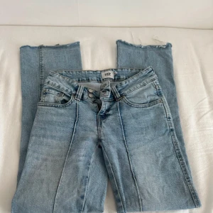Ljusblå lågmidjade flare bootcut jeans - Säljer ett par ljusblå lågmidjade utsvängda jeans från 157 Paris med raka ben och råa, avklippta benslut. Klassisk femficksmodell med hög midja och snygga söm-detaljer framtill. Perfekta för en avslappnad och trendig look.