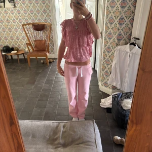 Glittrig rosa volangblus - Supersöt rosa blus med glittriga paljetter och volanger. Blusen har korta ärmar och en lös passform som ger en luftig känsla. Perfekt för dig som vill sticka ut med en färgglad och festlig topp!