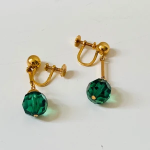 Förgyllda örhängen med gröna pärlor - Unika vintage örhängen med skruvstängning i förgylld metall och hängande, facetterade gröna pärlor. De har en cool retrovibe och passar dig som gillar att sticka ut med färg och detaljer. Perfekt för dig som vill ha örhängen utan hål i öronen. Stämpel Ad
