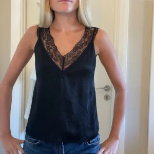 Svart linnetopp med spetsdetalj - Svart linnetopp med djup v-ringning och bred spetskant runt halsen. 