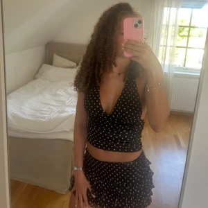 Svart prickigt set  - Säljer ett snyggt prickigt set som passar perfekt till fina tillfällen. Kjolen har inbyggda shorts som gör den mycket bekväm. Toppen är en halterneck med öppen rygg. 