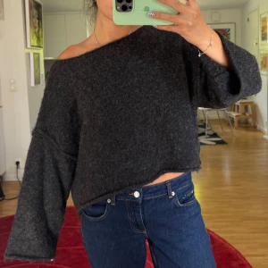 Mörkgrå offshoulder stickad tröja - Mysig mörkgrå stickad tröja med offshoulder och loose passform. Tröjan har vida, långa ärmar och är lite croppad i modellen
