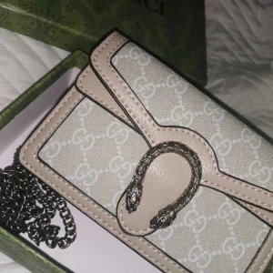 Beige Gucci Dionysus axelväska - Hej! Äkta Snygg beige Gucci Dionysus axelväska med silverfärgad kedja och ikoniskt spänne med ormdetaljer. Väskan har GG-mönster över hela ytan och är tillverkad i en mix av skinn och canvas. Perfekt storlek för det viktigaste och ger en lyxig vibe till din outfit. Helt ny! Köptes av mitt ex därför säljs den!🥰pris kan diskuteras via snabbköp. Kommer med kvitto, och original paket. 