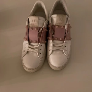 Valentino Rockstud sneakers vit/rosa - Snygga Valentino Rockstud sneakers i vitt skinn med breda ljusrosa band och ikoniska nitar över vristen. Är osäker på äktheten då dom är köpta på vinted och fanns inget kvitto eller låda till. 