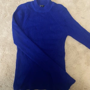 Blå ribbad stickad tröja Gina Tricot - Säljer en snygg blå stickad tröja från Gina Tricot i storlek M. Tröjan är ribbstickad med lång ärm och har en högre rund halsringning. Perfekt för dig som gillar en enkel men stilren look med lite edge. Den är figur syd och har ett snitt längst ner på armen.