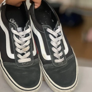 Svarta Vans Old Skool sneakers - Klassiska Vans Old Skool sneakers i svart med vit sidorand och vita snören. Ovandel i canvas och mocka, låg modell med platt gummisula och rund tå. Perfekta för en avslappnad streetstyle-look. Tyget lite blekt men inga hål eller fläckar finns 