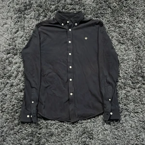 Svart skjorta från Morris, storlek S - Klassisk mörkblå skjorta från Morris med vita knappar och broderad logga på bröstet. Skjortan har button down-krage och är tillverkad i mjuk bomull. Perfekt passform stilren look.