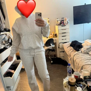 Grå hoodie med huva och ficka - Säljer hela settet för 400kr nypris för hela settet runt 700kr xs i byxor S i tröja  Mysig ljusgrå hoodie med huva och stor magficka. Tröjan har en relaxed passform och är tillverkad i mjuk bomullsmix, perfekt för chill dagar. Långa ärmar och ribbade muddar ger en klassisk look. Snygg att matcha med mjukisbyxor för en avslappnad stil. 