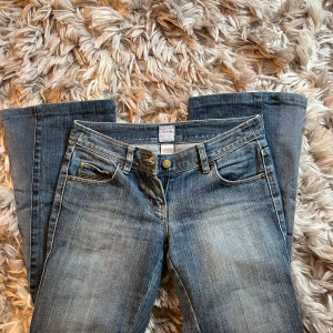 Blå jeans från Sass & Bide - Snygga blå jeans från Sass & Bide med klassisk femficksdesign och guldfärgade detaljer vid fickorna. Jeansen har en rak passform och subtila slitningar för en cool, avslappnad look. Perfekta till sneakers eller boots. Eftersom att det är vintage kan slitage tillkomma. 