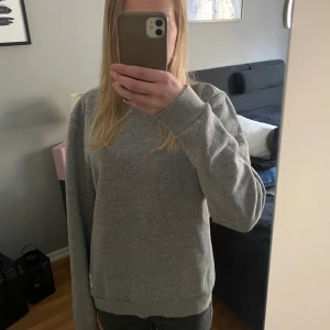 Grå sweatshirt  - Säljer en klassisk grå sweatshirt. Tröjan har rund halsringning, långa ärmar och en liten logotyp nertill. Perfekt för en avslappnad och stilren look.