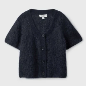 Mörkblå fluffig kofta från COS - Kortärmad, mörkblå kofta från COS i fluffigt material med v-ringning och knappar framtill. Perfekt att styla över en topp eller klänning för en trendig look.