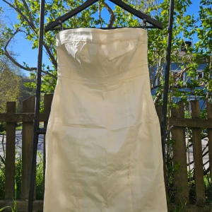 Vit axelbandslös klänning - Säljer en stilren vit klänning. Klänningen har en figurnära passform och är tillverkad i ett glansigt material som ger en elegant känsla. Perfekt för speciella tillfällen.