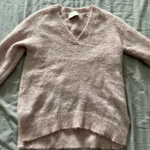 Ljusrosa stickad tröja - Supermjuk och fluffig ljusrosa stickad tröja från Neo Noir. Tröjan har v-ringad hals, långa ärmar och ribbade muddar vid ärmslut och nederkant. Perfekt för lager-på-lager och en mysig look.