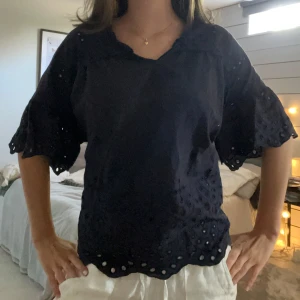 Super söt blus 💕 - Säljer en svart mörkblå blus med vackra broderade håldetaljer och vida, korta ärmar. Blusen har en lös passform och vågig kant nertill och vid ärmslut. Det är min spegel som är smutsig EJ tröjan☺️