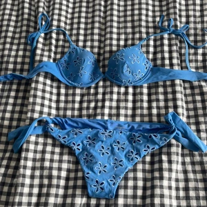 Blå bikini från Calzedonia med blommigt broderi - Säljer en blå bikini från Calzedonia med knyt i sidorna och axelbanden. Överdel och underdel har broderade blommor som ger en söt och somrig känsla. Perfekt för stranden eller poolen!