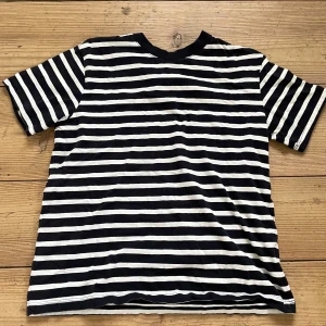 Svartvit randig t-shirt från H&M - Klassisk svartvit randig t-shirt från H&M. T-shirten har korta ärmar och rund halsringning. Perfekt för en avslappnad stil och enkel att matcha med jeans eller shorts.