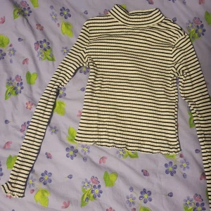 Randig ribbad polotröja - Säljer en ribbad långärmad polotröja med svarta och vita ränder. Tröjan har en hög krage och är croppad i modellen. Perfekt för dig som gillar en trendig och bekväm stil.