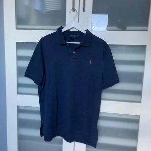 Mörkblå pikétröja från Ralph Lauren - Säljer en stilren mörkblå pikétröja från Ralph Lauren. Tröjan har en klassisk krage och korta ärmar, perfekt för en avslappnad men ändå elegant look. Tillverkad i mjukt Pima-bomullsmaterial för extra komfort. Kan gå ner i pris vid snabb affär