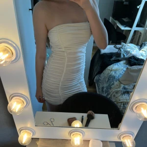 Vit tight kortklänning med rynkade detaljer - Säljer en vit tight kortklänning med rynkade detaljer och axelband. Klänningen har en rak halsringning och är figurnära, perfekt för dig som vill ha en stilren och trendig look. Man kan välja att ha framme banden eller inte, har en liten fläck, går antagligen lätt bort i tvätten.