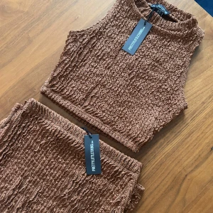 Brun croppad linnetopp från PrettyLittleThing - Säljer en brun croppad linnetopp från PrettyLittleThing. Toppen är ärmlös och har en strukturerad, ribbad yta. Perfekt att matcha med kjol eller byxor för en trendig look.