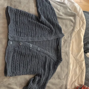 Grå stickad kofta från KappAhl - Säljer en grå stickad kofta från KappAhl i storlek S. Koftan har ett virkat mönster, v-ringning och tre knappar framtill. Perfekt att slänga över en topp för en chill look.