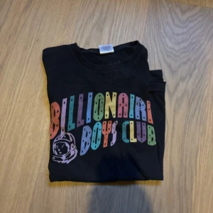 Svart t-shirt från Billionaire Boys Club - Säljer en svart t-shirt från Billionaire Boys Club med färgglatt tryck på bröstet och astronaut-logga. T-shirten är i 100% bomull och har en klassisk passform med korta ärmar. Perfekt för dig som gillar streetwear och vill sticka ut med en ikonisk design.