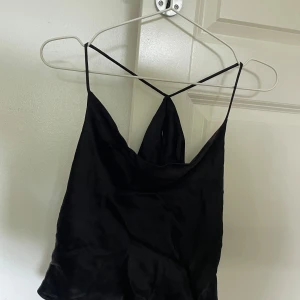 Svart satinlinne med tunna axelband från Zara - Säljer ett svart satinlinne från Zara med tunna axelband som korsas i ryggen. Linnet har en elegant, något lös passform och en lätt glansig yta. Perfekt att styla till olika outfits!