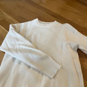 Vit stickad tröja från Zara - Säljer en enkel och stilren vit stickad tröja från Zara. Tröjan har rund halsringning och långa ärmar med ribbade muddar. Perfekt för lager-på-lager och passar till många olika outfits.