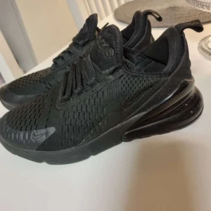 Nike Air Max 270 helsvarta sneakers - Säljer ett par helsvarta Nike Air Max 270 sneakers med luftig mesh-ovandel och stor synlig Air-enhet i hälen. Skorna har snörning och diskreta Nike-loggor på sidorna. Perfekta för dig som gillar sportig och stilren look. Säljes då lillebror inte kunde ha dem, i nästan oanvändt skick.