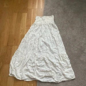 Vit lång kjol  - Säljer en vit lång kjol med smockad överdel och vid kjol och har en luftig känsla, perfekt för varma dagar. Passar till sommarens alla tillfällen!