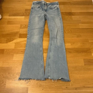Ljusblå bootcut jeans med råa kanter - Ljusblå jeans med bootcut passform och råa, fransiga benslut. Klassisk femficksmodell i denim med slitna detaljer och låg midja. Perfekta för en avslappnad och trendig look. Defekt på sista bilden, går enkelt att fixa.