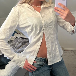 Vit skjorta med diskret rutmönster - Säljer en klassisk vit skjorta med subtilt rutmönster. Skjortan har lång ärm, krage och knappar framtill. Perfekt att styla med jeans eller kjol för en clean look. Materialet känns lätt och luftigt.