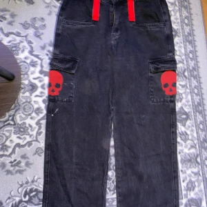 Jeans - Coola Jeans med röda detaljer. Har en liten fläck med vit färg på höger lår