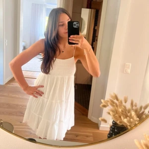 Vit sommarklänning med smala axelband - Säljer en söt vit klänning med smala axelband och lätt volang i kjolen. Klänningen är ärmlös och har en luftig passform, perfekt för varma dagar. Materialet känns lätt och somrigt.