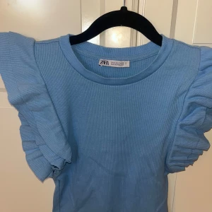Blå ribbad topp med volangärmar från Zara - Supersöt ljusblå ribbad topp från Zara med volangdetaljer på ärmarna. Perfekt för vår och sommar.Mjuk och stretchig bomullskvalitet. Inga defekter, super fint skick💗
