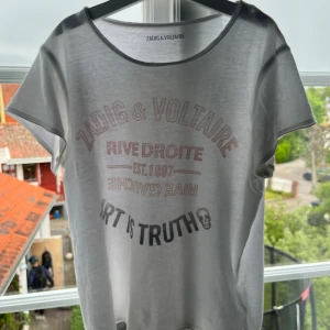 Vit t-shirt med tryck från Zadig & Voltaire - Vit t-shirt från Zadig & Voltaire med tryck i svart och rosa framtill: 'Zadig & Voltaire', 'Rive Droite', 'Art is Truth' och en liten döskalle. Klassisk rund hals och korta ärmar. Perfekt för en cool och avslappnad stil. Säljer då den är för liten! Storlek 14a som är ungefär storlek 160-170 🩷