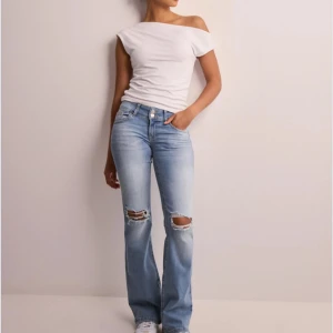 Ljusblå bootcut jeans med slitningar från Nelly - Säljer ett par ljusblå bootcut jeans från Nelly med slitningar på knäna och dubbla knappar i midjan. Jeansen har klassiska bakfickor med lock och knapp, samt en snygg utsvängd passform.