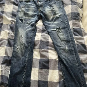 Blå slitna jeans från Dsquared2 - Säljer ett par blå jeans från Dsquared2 med slitningar och hål för en riktigt cool look. Jeansen har klassisk femficksmodell och normal passform. Perfekta för dig som gillar streetstyle och vill sticka ut.