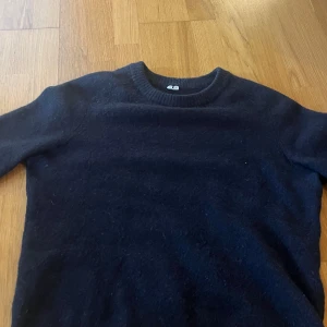 Mörkblå stickad tröja - Arket  - Säljer en enkel och stilren mörkblå stickad tröja i storlek M. Tröjan har rund halsringning och långa ärmar med ribbade muddar. Perfekt för kyligare dagar och lätt att matcha med olika outfits.