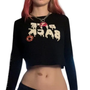Svart croppad långärmad topp med tryck - Svart croppad långärmad topp med texten 'BITE BACK' i  glittrigt vitt och ett glittrigt rött läpp-tryck med vampyrtänder framtill. Ena ärmen har vitt tryck längs sidan. Perfekt för dig som gillar edgy streetstyle. Barnstorlek men passar mig som brukar ha xs/s