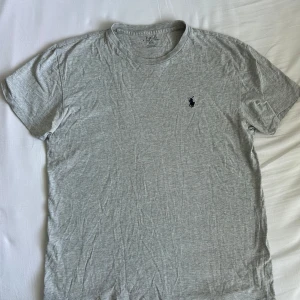 Grå t-shirt från Polo Ralph Lauren - Säljer en klassisk grå t-shirt från Polo Ralph Lauren med liten broderad logga på bröstet. T-shirten har rund halsringning och är kortärmad. Perfekt basplagg i mjuk bomull.